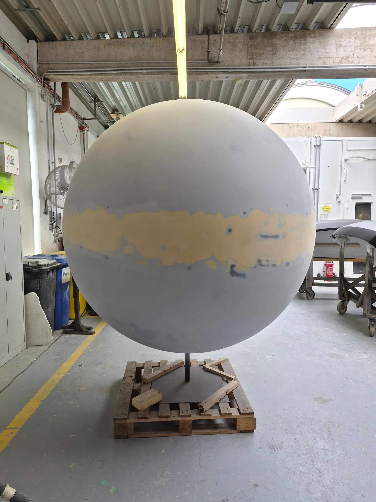 Large raw grey primer sphere on a stand in a fabrication workshop